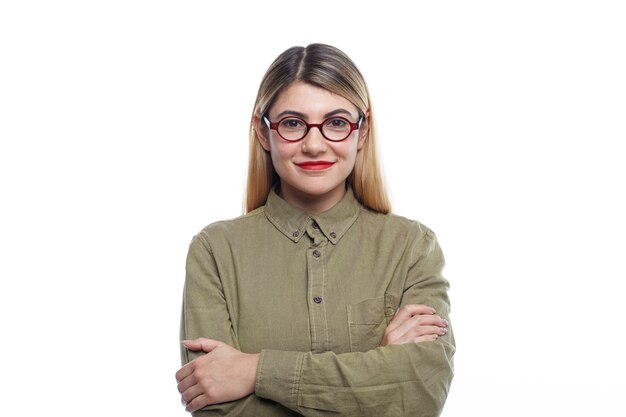 Tour de taille d'une jeune femme européenne attrayante positive employée ou étudiant portant du rouge à lèvres et des lunettes ovales souriant avec confiance, gardant les bras croisés, posant isolé