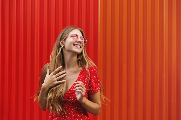 Tourisme Heureuse femme mangeant de la crème glacée sucrée à l'extérieur et regardant à droite souriant joyeuse debout près du mur rouge Voyageuse explorant la ville en vacances