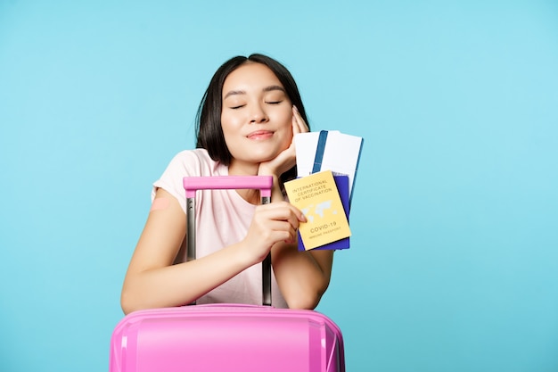 Photo gratuite une touriste asiatique rêveuse et souriante pense à voyager avec un passeport et des billets...