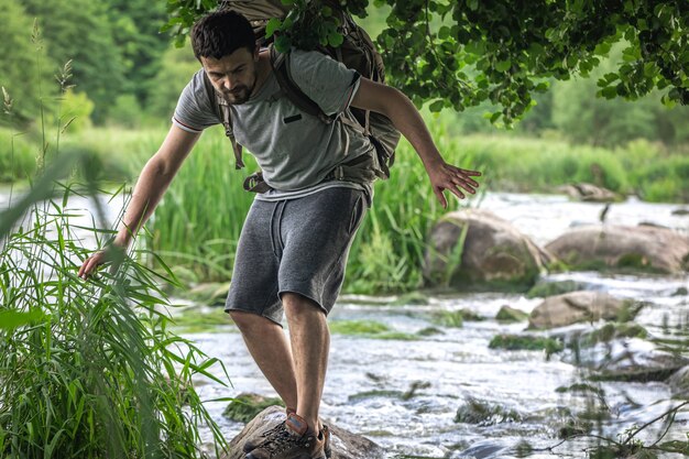 Un touriste avec un grand sac à dos de randonnée se rafraîchit près d'une rivière de montagne dans la chaleur estivale.