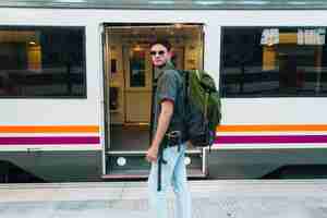 Photo gratuite touriste mâle élégant portant des lunettes et sac à dos portant debout devant le train