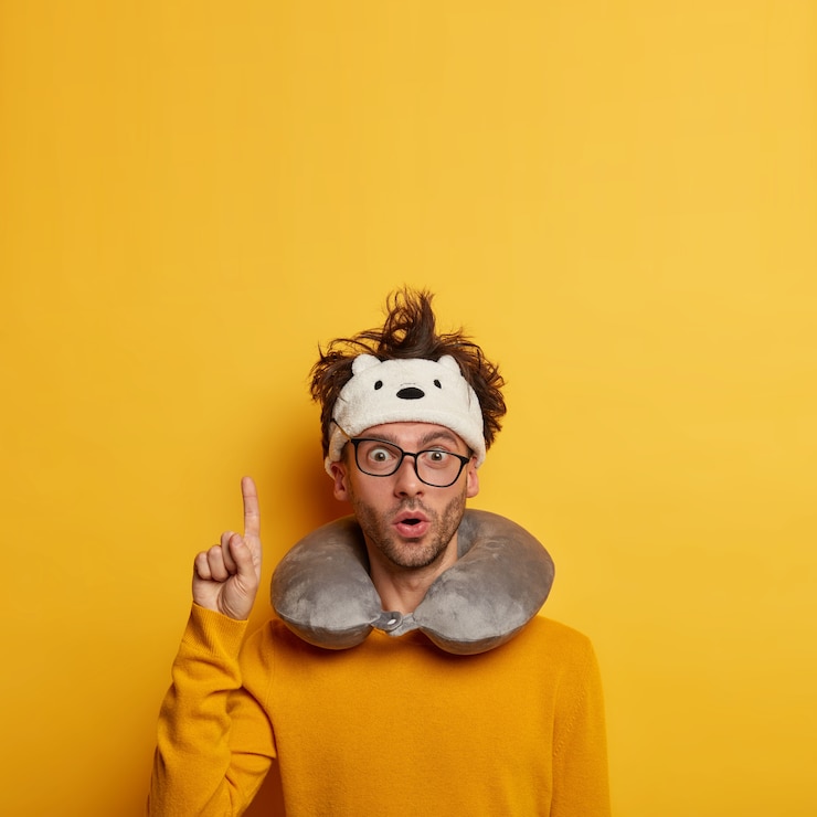 Photo gratuit un touriste masculin surpris pose dans la salle d'attente, porte un oreiller autour du cou, a une expression de visage choquée