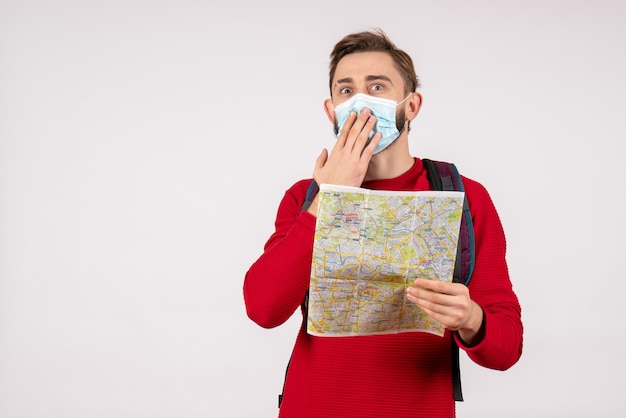 Touriste masculin vue de face dans un masque stérile tenant une carte sur un mur blanc