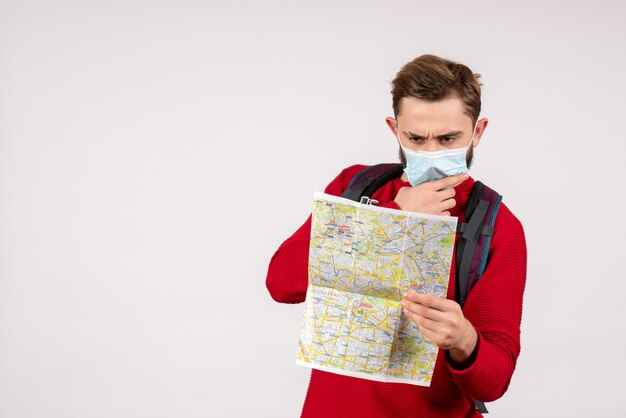 Touriste masculin vue de face en masque stérile explorant la carte sur le mur blanc