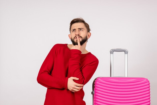 Touriste masculin vue de face avec un sac rose pensant sur un mur blanc