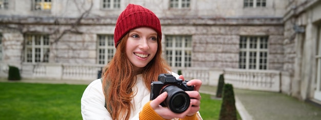 Photo gratuite une touriste rousse heureuse prend des photos avec un appareil photo professionnel et se promène dans la ville et