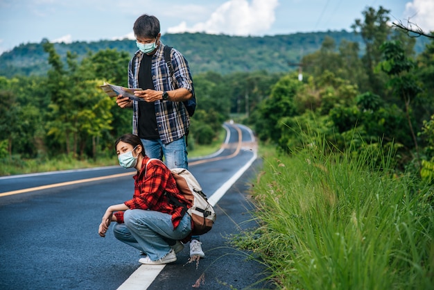 Touristes assis, touristes masculins regardant la carte, tous deux portant des masques et sur le bord de la route.