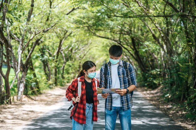 Les touristes masculins et féminins portent des masques médicaux et regardent la carte dans la rue.