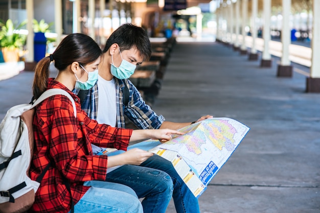 Les touristes masculins et féminins regardent la carte à côté de la voie ferrée.