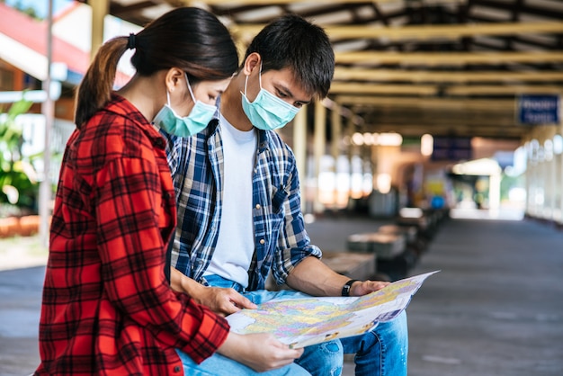 Les touristes masculins et féminins regardent la carte à côté de la voie ferrée.