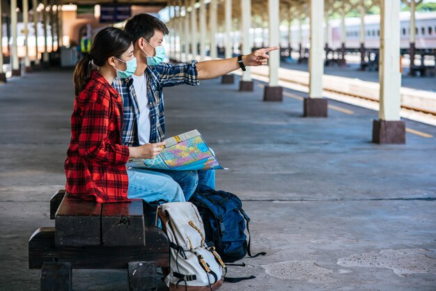 Les touristes masculins et féminins regardent la carte à côté de la voie ferrée.
