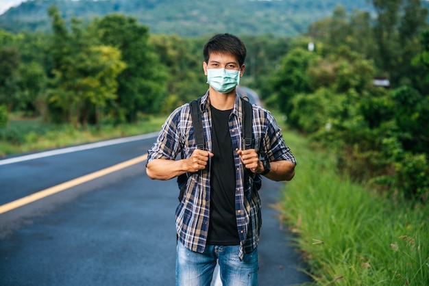 Les Touristes Masculins Portant Un Masque, Portant Un Sac à Dos Sur La Route.