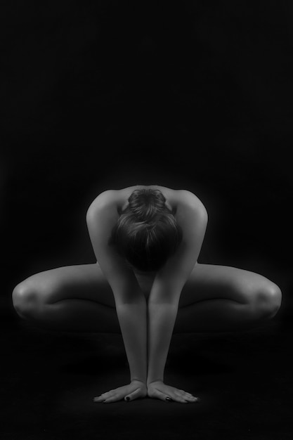 Photo gratuite tourné en noir et blanc d'une jeune femme nue en équilibre sur ses mains et ses jambes