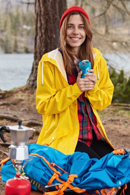 Tourné en plein air d'une femme européenne avec une expression joyeuse, se dresse sur les genoux au sol dans la forêt près de la rivière