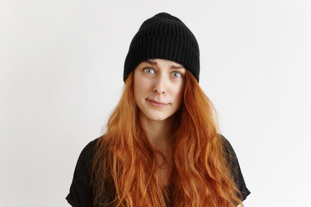 Tourné en studio intérieur de jolie fille rousse hipster portant un t-shirt et un chapeau ayant un regard indigné et blâmant