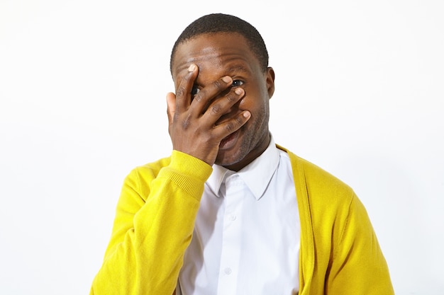 Tourné en studio isolé de séduisant jeune homme afro-américain dans des vêtements élégants couvrant le visage avec la paume, riant de situation ridicule drôle. Languette corporelle, expressions humaines, gestes et signes