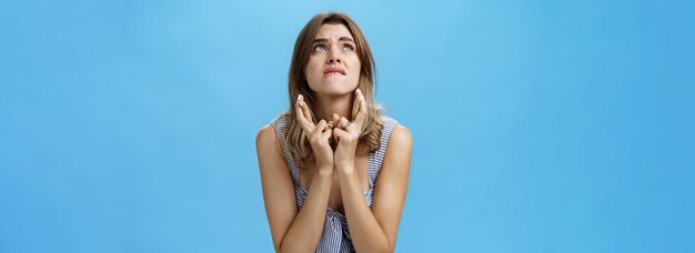 Tourné à la taille d'une jeune femme mignonne intense qui croise les doigts en se mordant la lèvre inférieure et en fronçant les sourcils