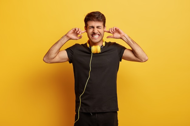 Tournez le volume, s'il vous plaît! Un jeune homme agacé se bouche les oreilles et serre les dents, insatisfait de la musique rock forte, ignore le bruit