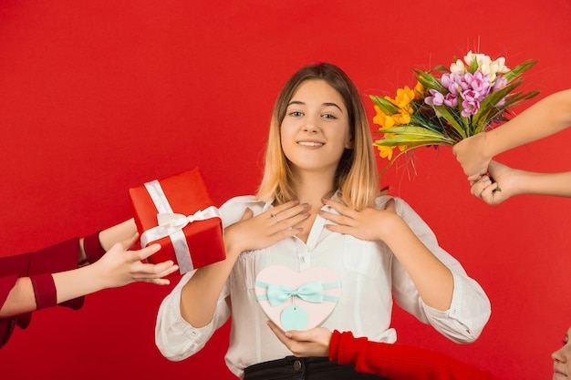 Tous les cadeaux et fleurs. Célébration de la Saint-Valentin. Heureuse, jolie fille caucasienne isolée sur fond de studio rouge. Concept d'émotions humaines, expression faciale, amour, relations, vacances romantiques.