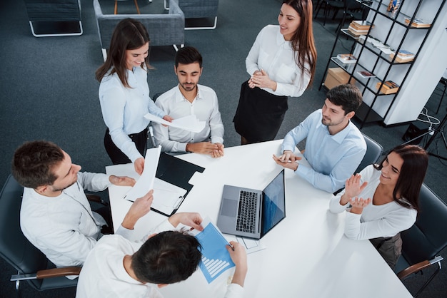 Tout le monde est de bonne humeur. Vue de dessus des employés de bureau en vêtements classiques assis près de la table à l'aide d'un ordinateur portable et de documents