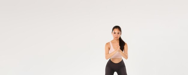 Toute la longueur d'une athelte féminine bien concentrée, une fille de fitness asiatique, effectue des squats avec un han serré