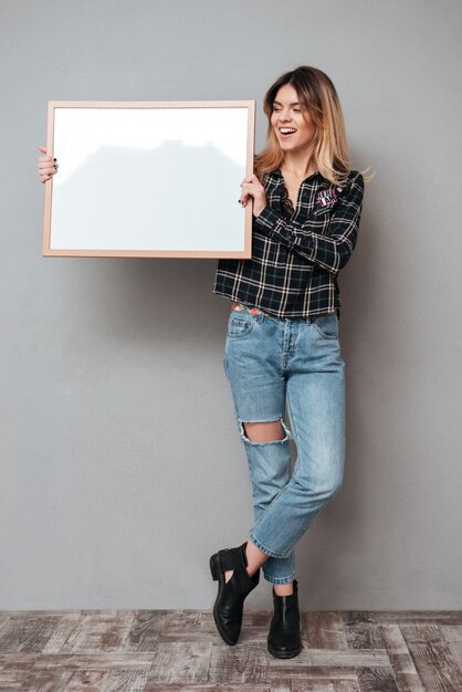 Toute la longueur d'une femme souriante tenant une planche vierge