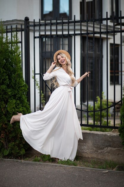 Toute la longueur de l'heureuse belle jeune femme vêtue d'une robe et marchant dans la rue en se tenant près d'une clôture. Concept de beauté et de mode