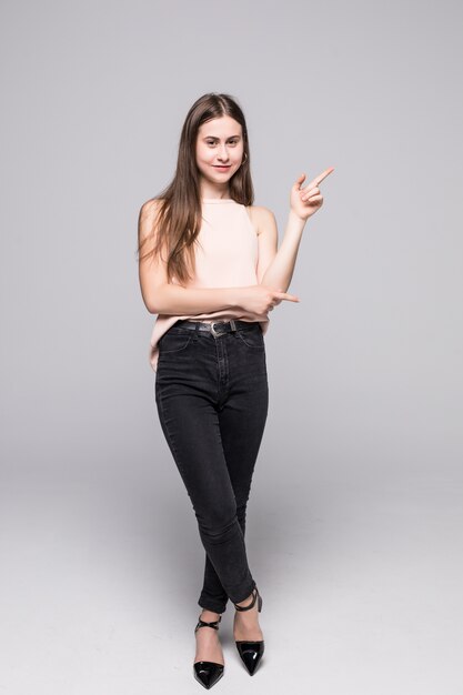 Toute la longueur de la jeune femme pointant vers le côté et regardant là-bas, isolé sur mur blanc