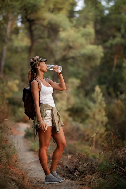 Toute la longueur de la randonneuse buvant de l'eau en se tenant debout sur un sentier dans la forêt