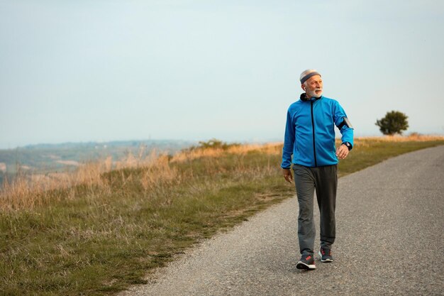 Toute la longueur d'un sportif senior se promenant le matin et écoutant de la musique sur des écouteurs dans la nature Espace de copie