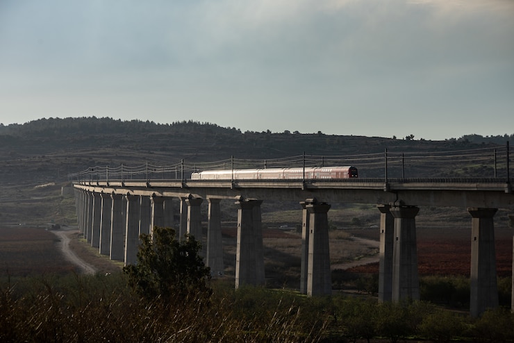 Photo gratuit train sur un chemin de fer entouré de verdure sous un ciel bleu nuageux pendant la soirée
