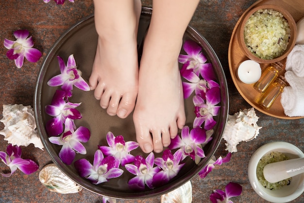 Traitement spa et produit pour pieds féminins et spa pour les mains. fleurs d'orchidées dans un bol en céramique.