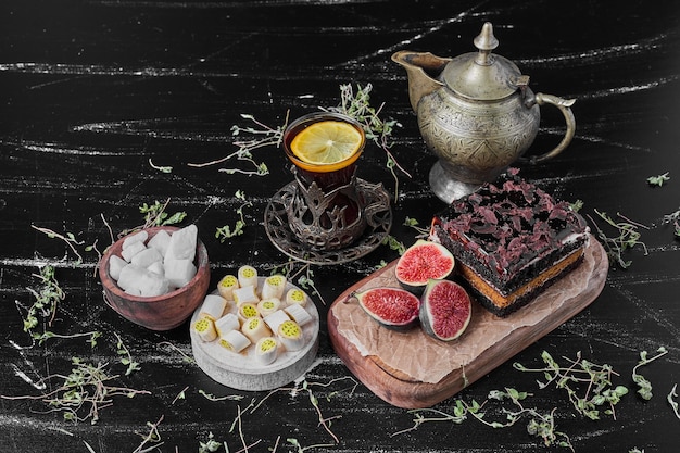 Photo gratuite une tranche carrée de gâteau au fromage au chocolat sur une planche en bois avec un verre de thé.