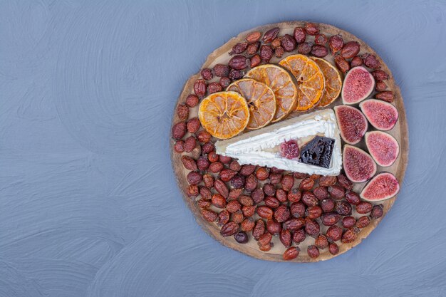 Une tranche de cheesecake dans un plateau de fruits avec figues, tranches d'orange et hanches