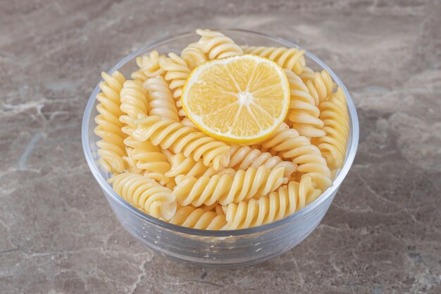 Une tranche de citron dans les pâtes fusilli sur le bol, sur la surface en marbre.