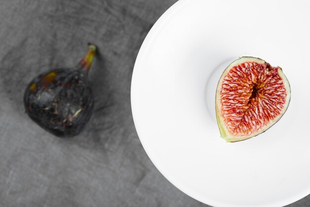 Une tranche de figue noire sur une assiette blanche à côté de figue entière. Photo de haute qualité