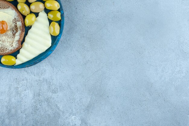 Tranche de fromage, beurre et olives vertes sur un plateau sur une table en marbre.