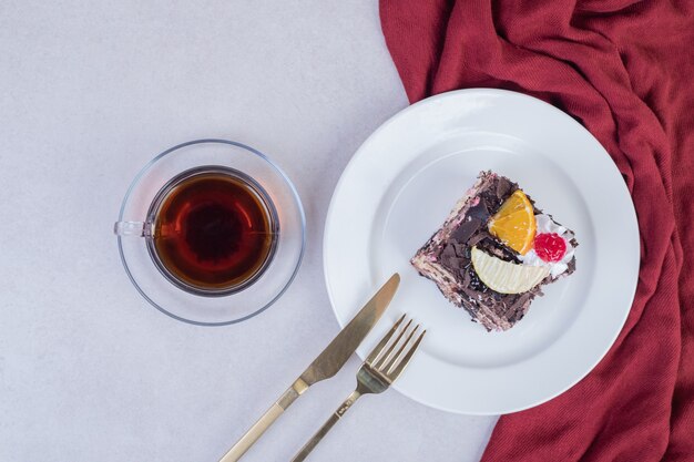 Tranche de gâteau au chocolat sur une plaque blanche avec une tasse de thé.