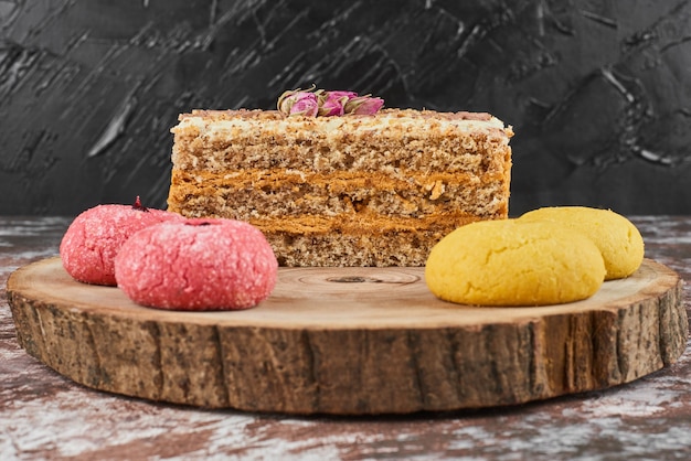 Tranche de gâteau aux carottes avec des biscuits sur une planche de bois.