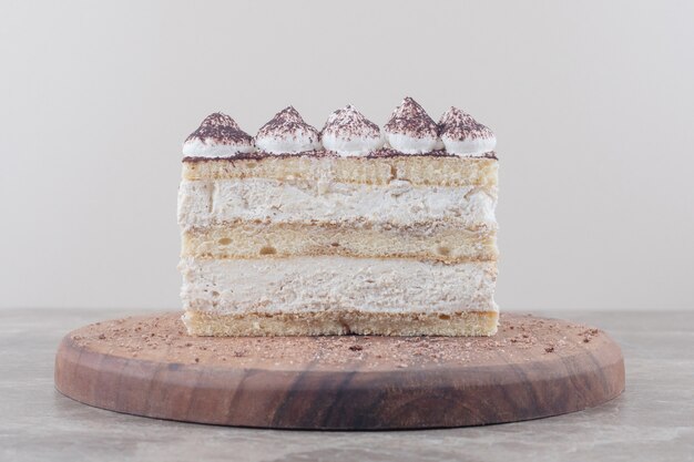 Tranche de gâteau garnie de crème et de cacao en poudre sur une planche sur marbre