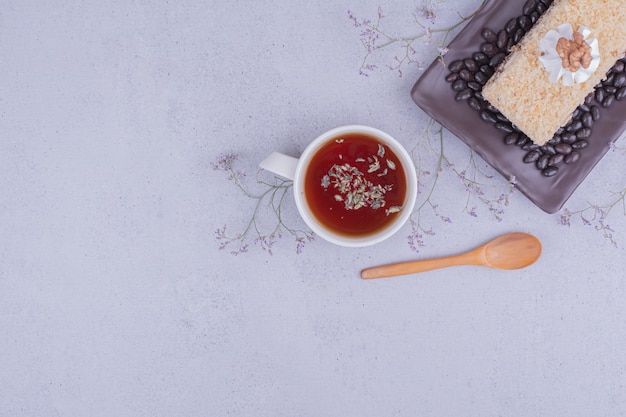 Une tranche de gâteau medovic avec des haricots au chocolat dans un plateau noir avec une tasse de thé