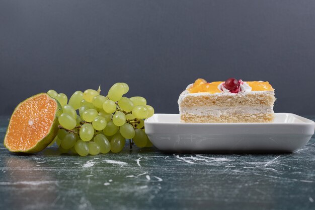 Photo gratuite tranche de gâteau, raisins et orange sur mur bleu.