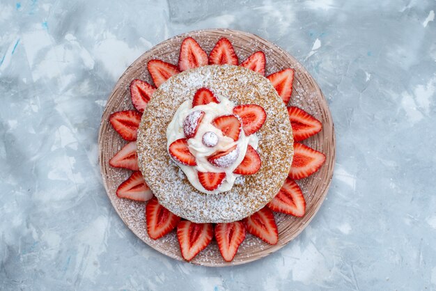 Une tranche de gâteau vue de dessus avec de la crème et des fraises rouges fraîches à l'intérieur de la plaque sur le fond bleu-gris