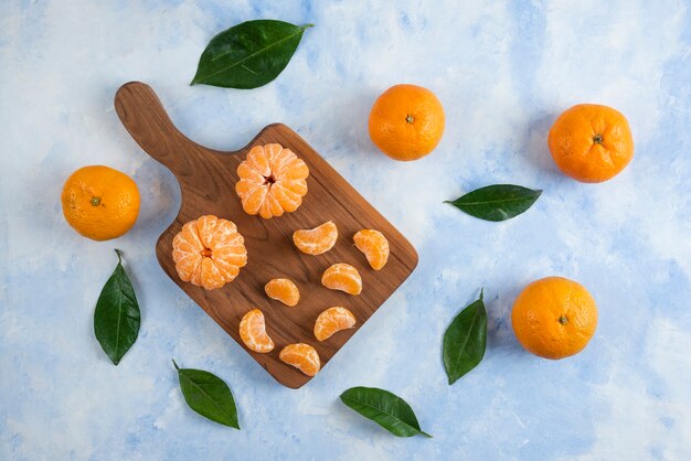 Tranche de mandarines clémentines entières et pelées. Sur planche de bois sur surface bleue