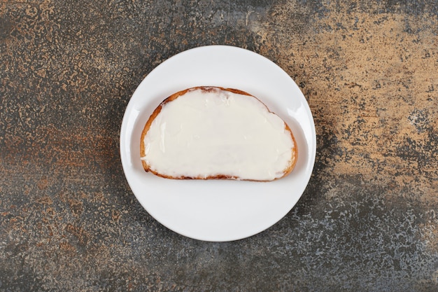 Tranche de pain grillé avec de la crème sure sur une assiette blanche.