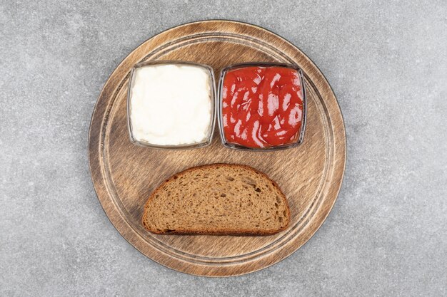 Tranche de pain noir, ketchup et mayonnaise sur planche de bois