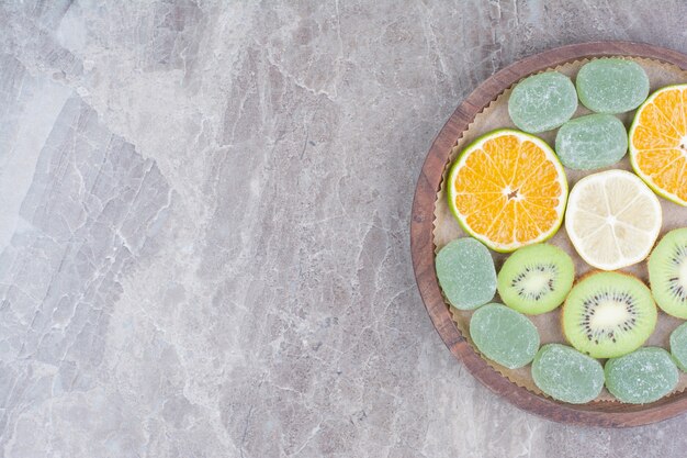 Tranches d'agrumes, kiwi et bonbons sur planche de bois.