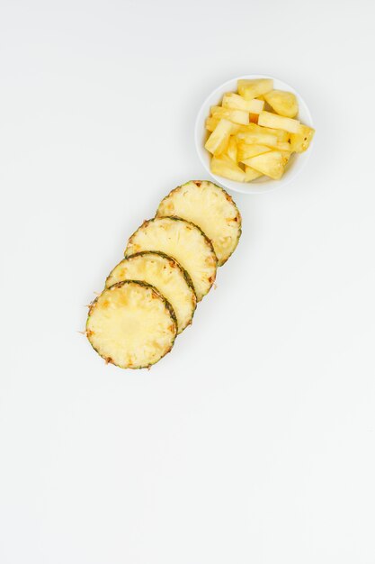 Tranches d'ananas frais dans un bol blanc sur un plat blanc.