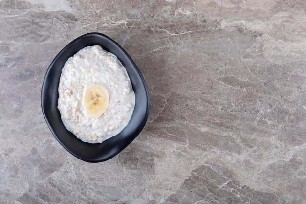 Tranches de banane mûre sur un bol de porridge, sur le fond de marbre.