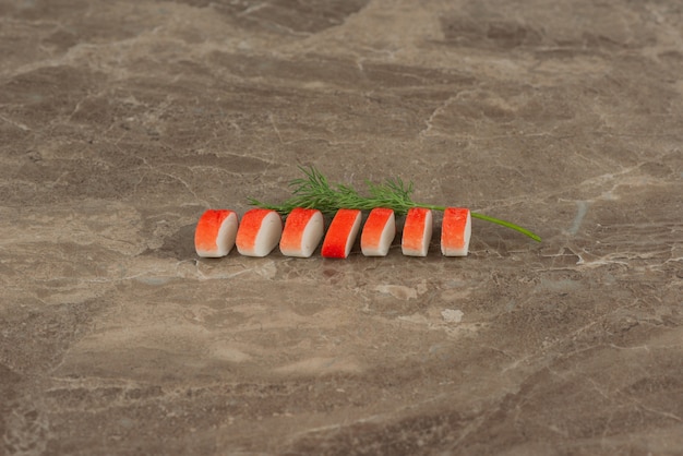 Tranches de bâtonnets de crabe avec des verts sur table en marbre.